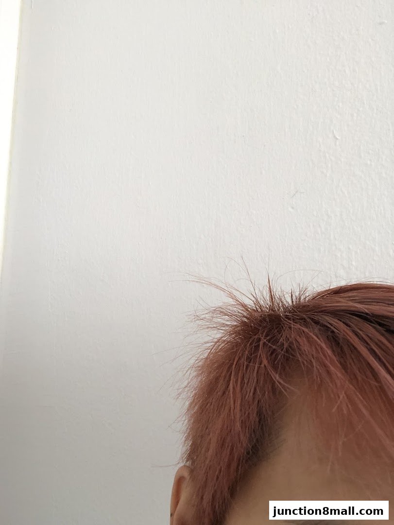 Close-up of a person's head with pinkish-brown hair against a white wall.