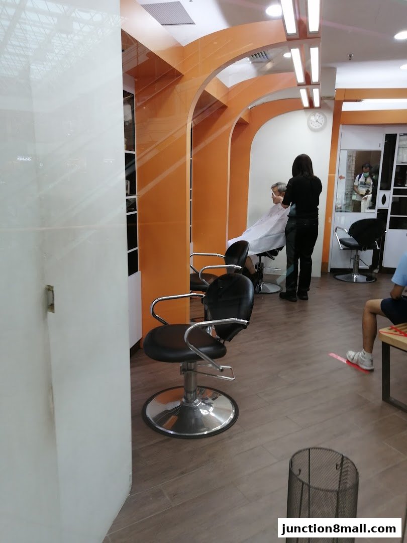 A barber is cutting a customer's hair inside a modern salon with orange accents.