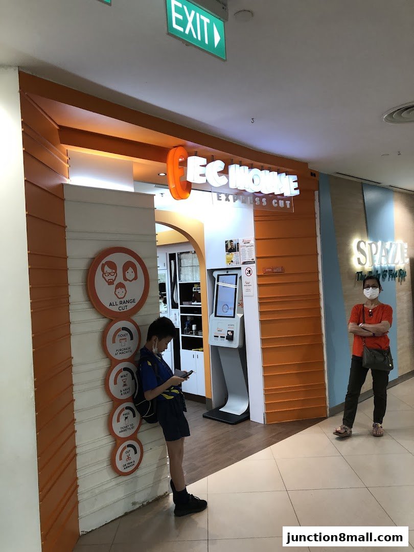 A young boy waits outside EC House Express Cut, a hair salon with an orange facade.