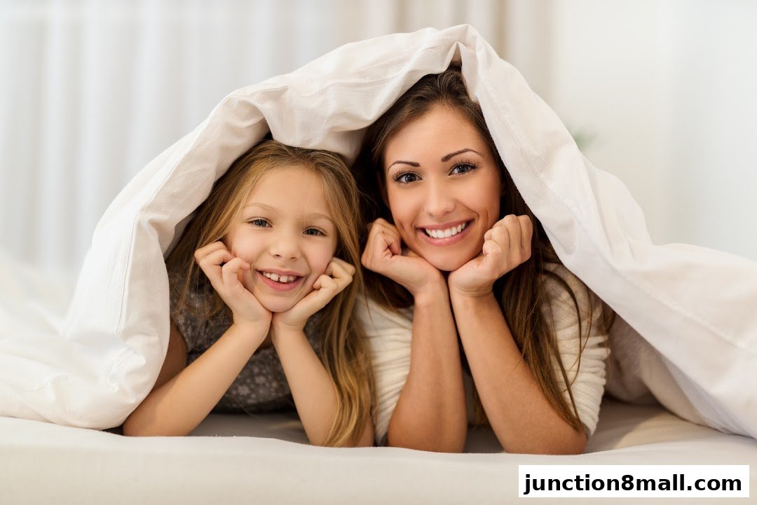 A mother and daughter smiling and peeking out from under a white duvet.