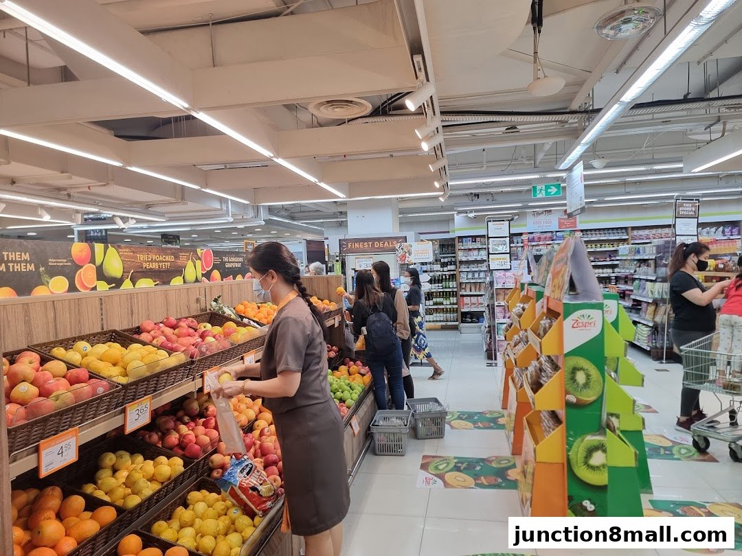 Shoppers browse fresh fruits and produce in a well-lit supermarket aisle.