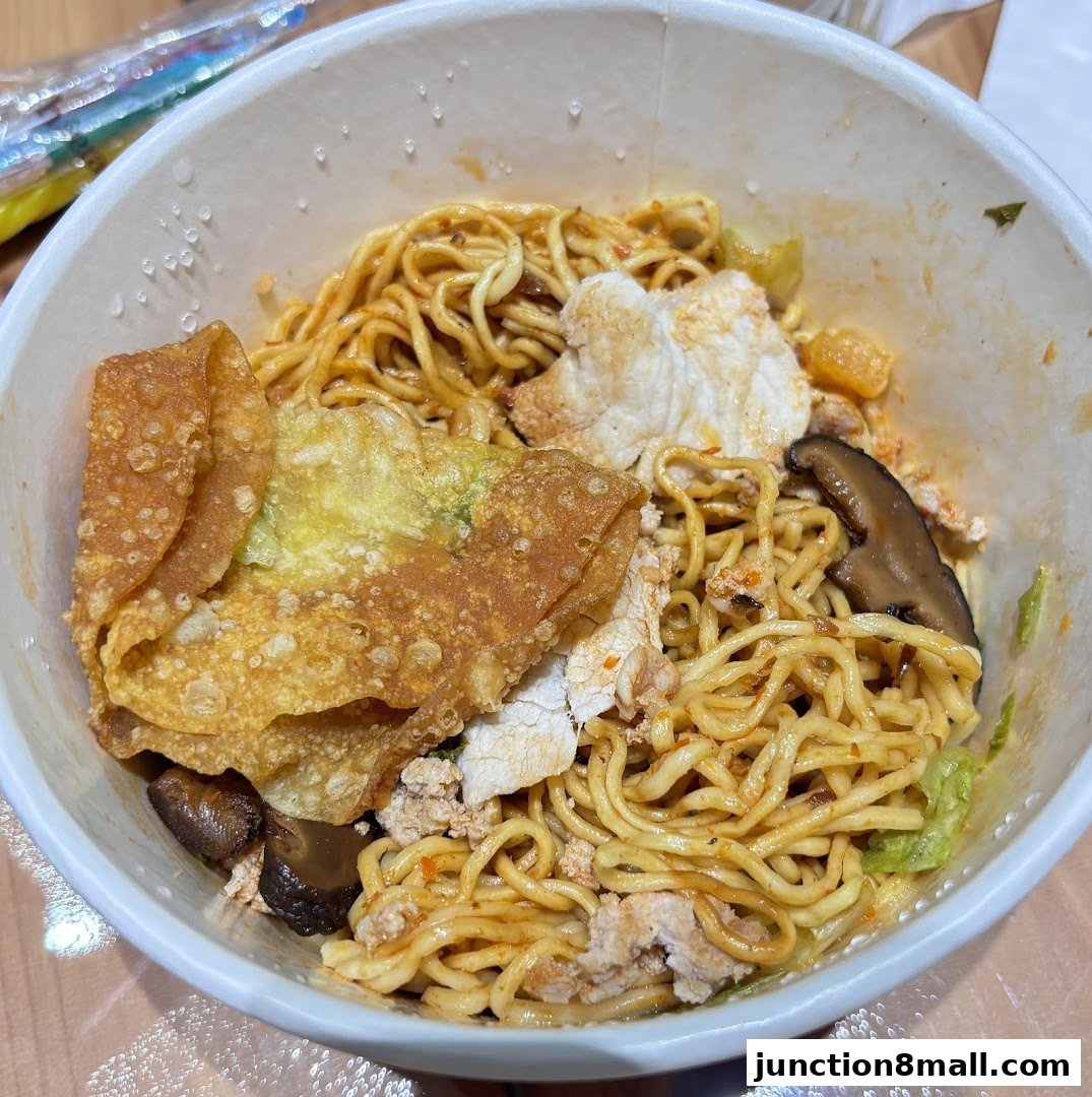 A close-up view of a bowl of noodles with wontons, mushrooms, and minced meat.
