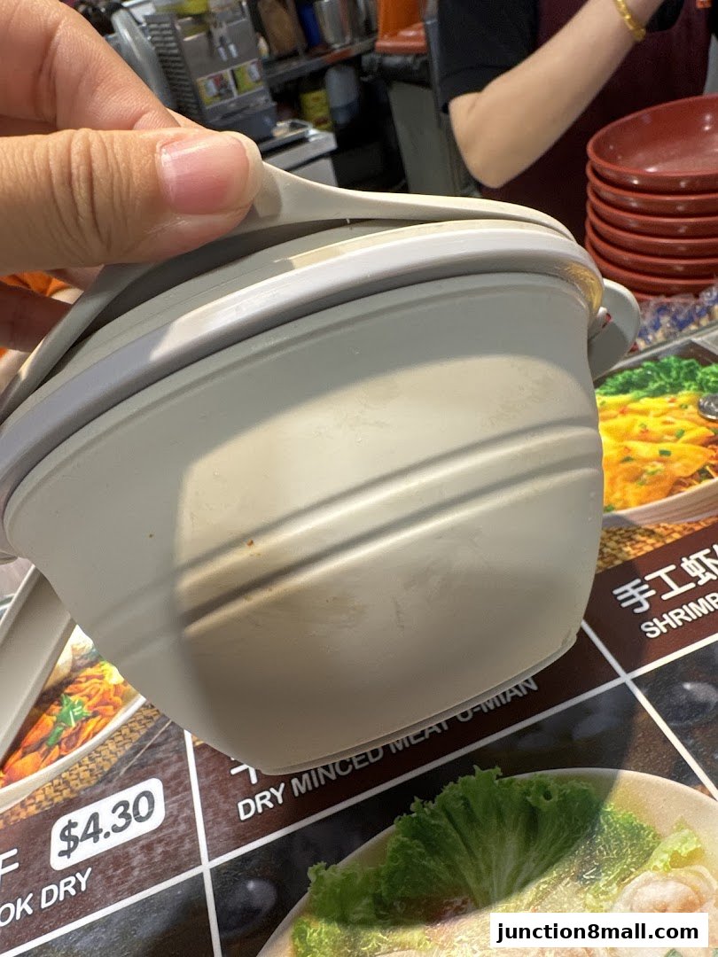 A hand holds a light grey bowl over a menu with food images and prices.