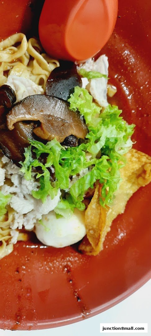 A close-up of a bowl of noodles with minced meat, mushrooms, lettuce, and a fried wonton.