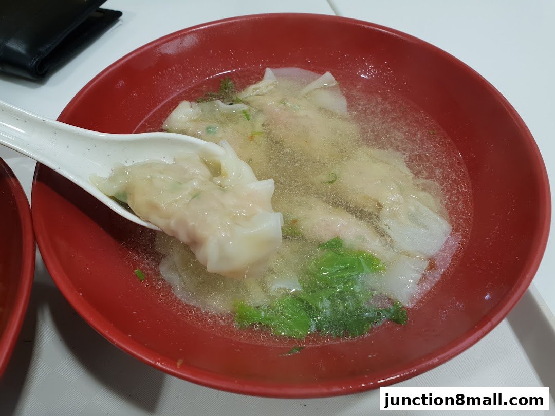 A close-up shot of a bowl of wonton soup with a spoon lifting a wonton.