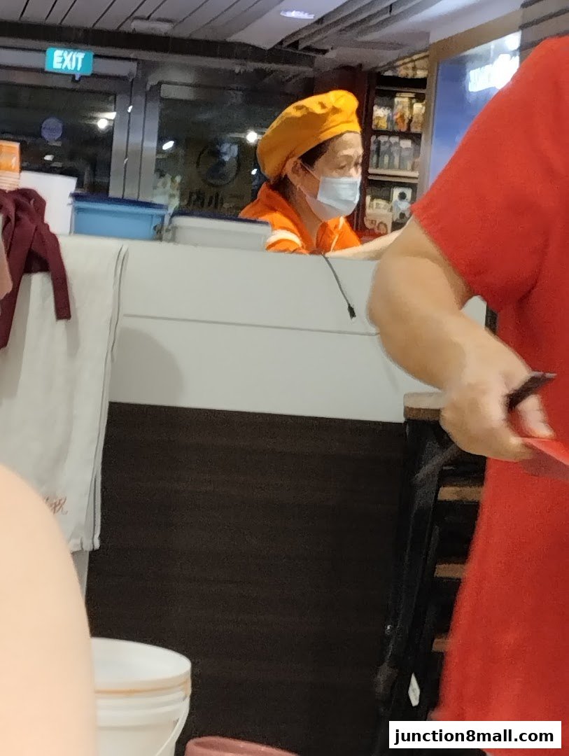 A staff member wearing a yellow hat and mask serves customers at Fei Siong.