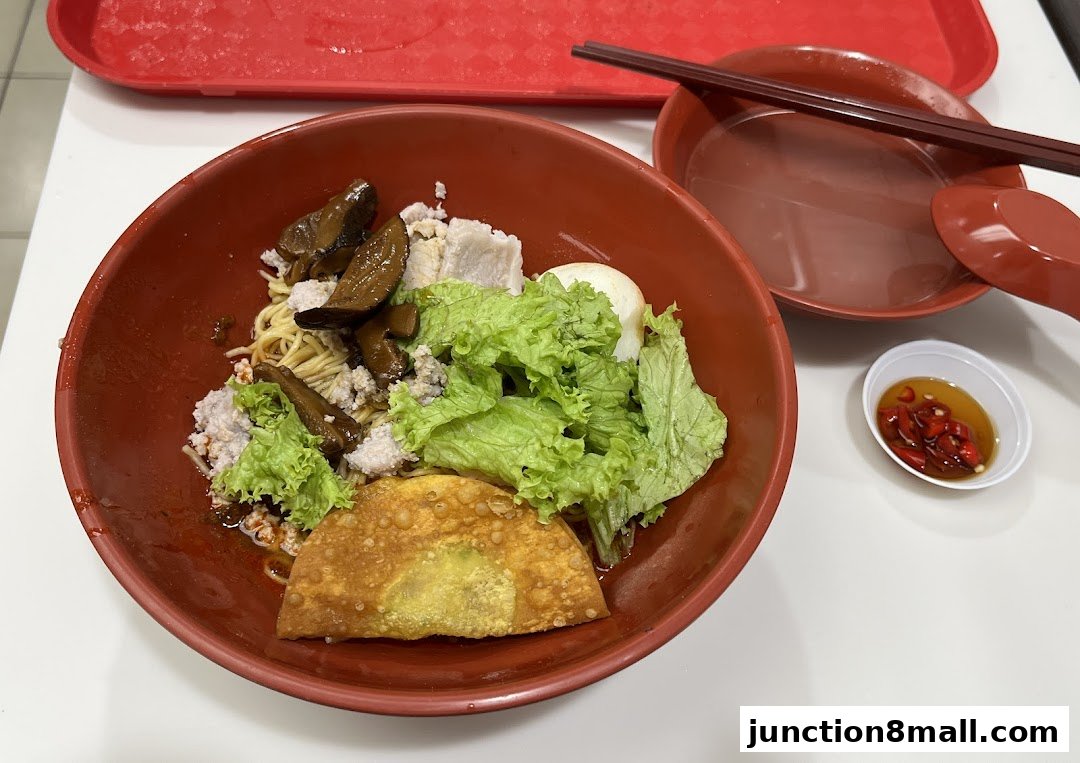 A bowl of noodles with minced meat, mushrooms, lettuce, and a fried wonton.