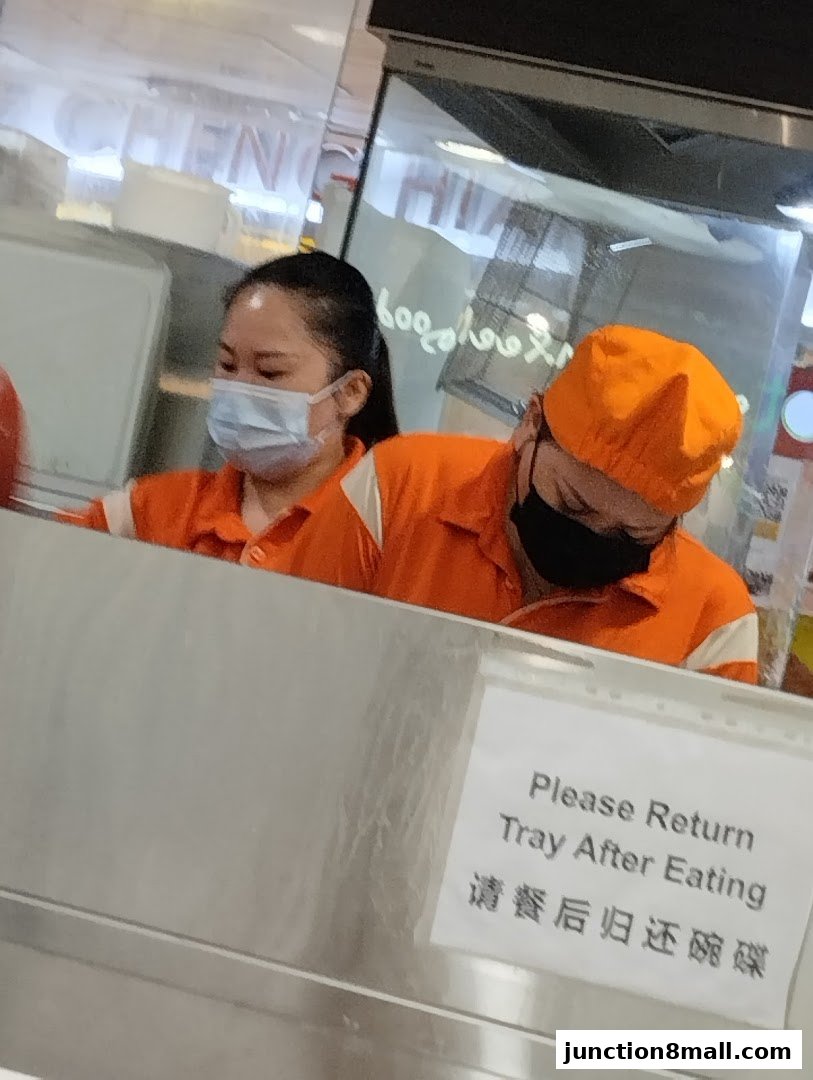 Two staff members in orange uniforms working behind a counter at Fei Siong.