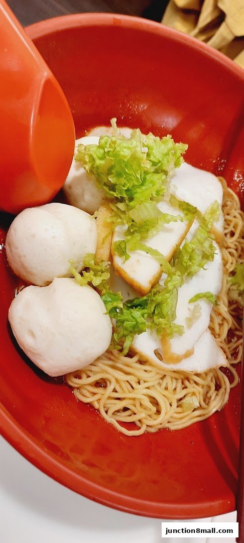 A close-up of a bowl of noodles with fish balls, fish cakes, and lettuce.