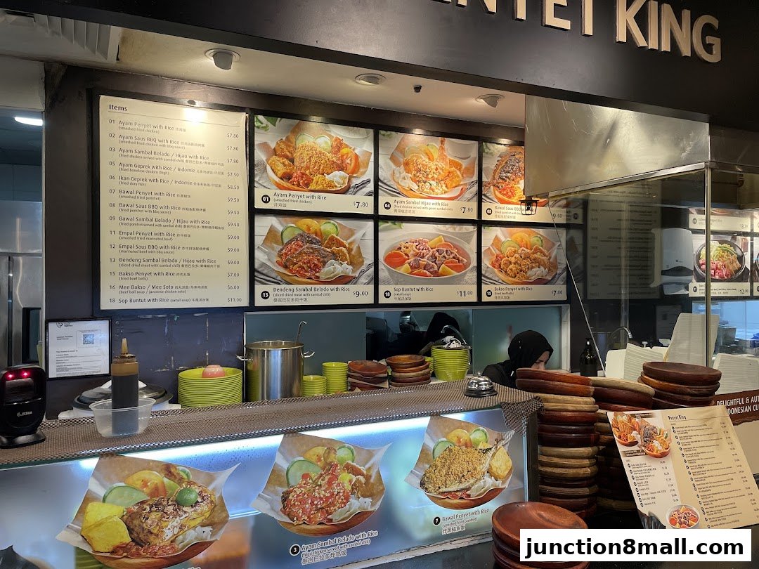 A food stall counter displaying a menu with pictures of Indonesian dishes and prices.