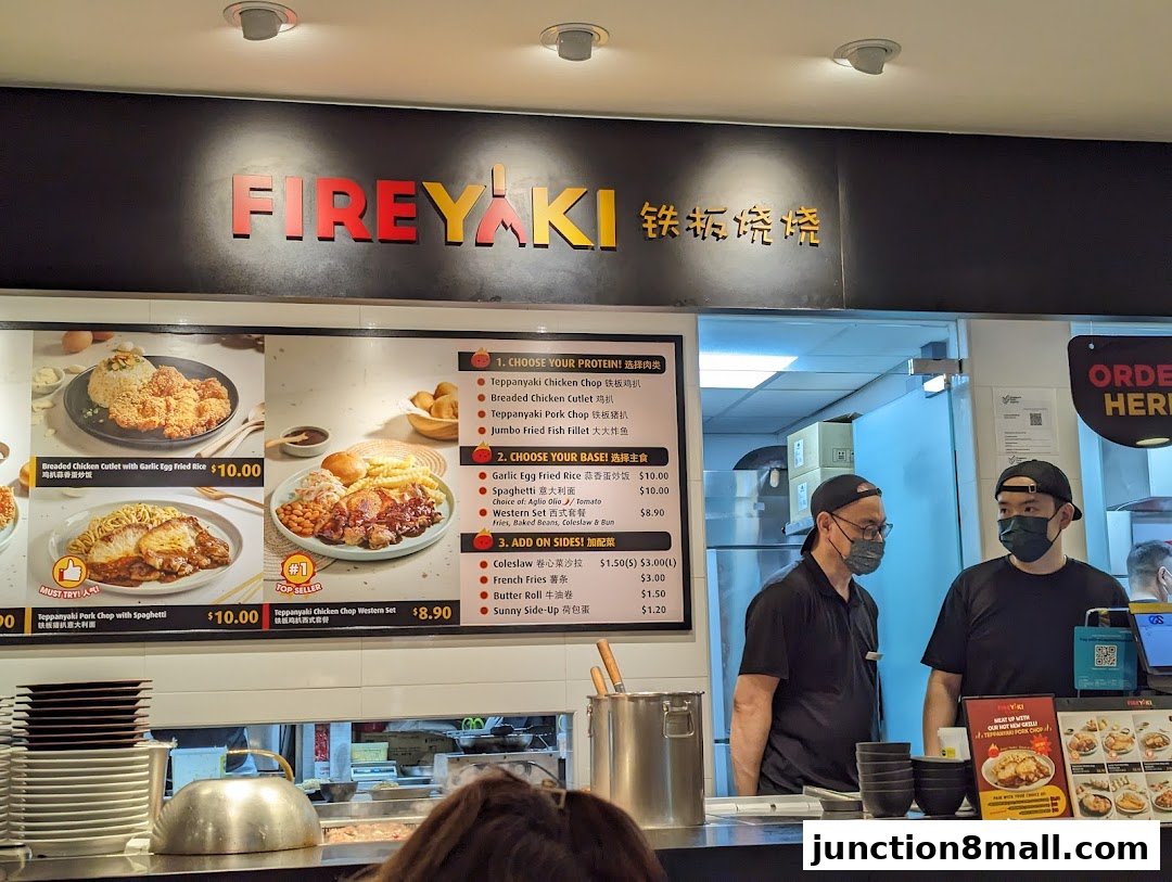 A food stall counter with a menu displaying various dishes and two staff members.
