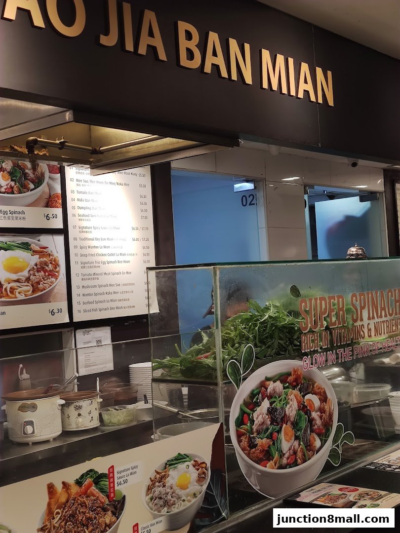 A food stall counter displaying a menu with various noodle dishes and a prominent advertisement for spinach.