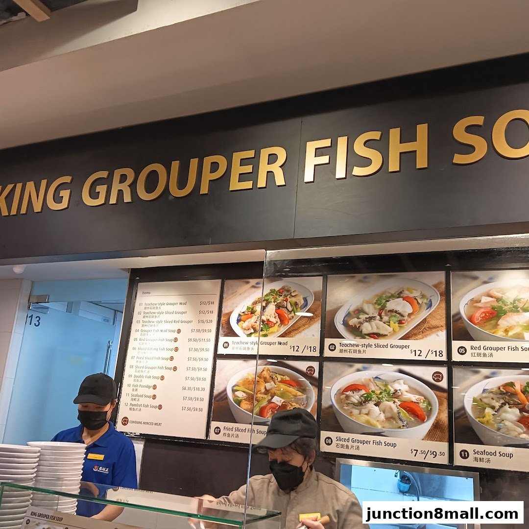 A food stall counter with a menu board displaying various fish soup dishes and pictures of the food.