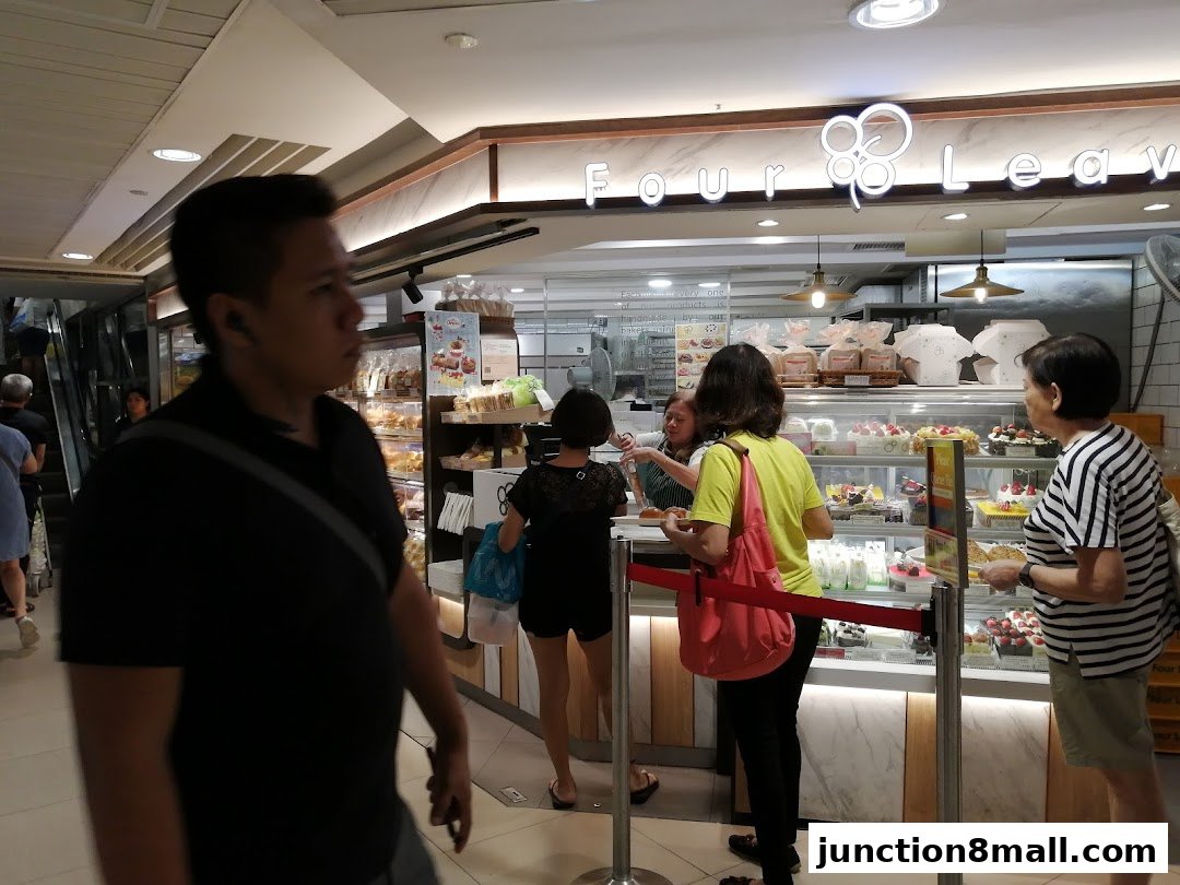 Customers are queuing at a bakery counter displaying various cakes and pastries.