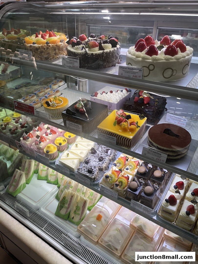A display case filled with various cakes, pastries, and sandwiches.