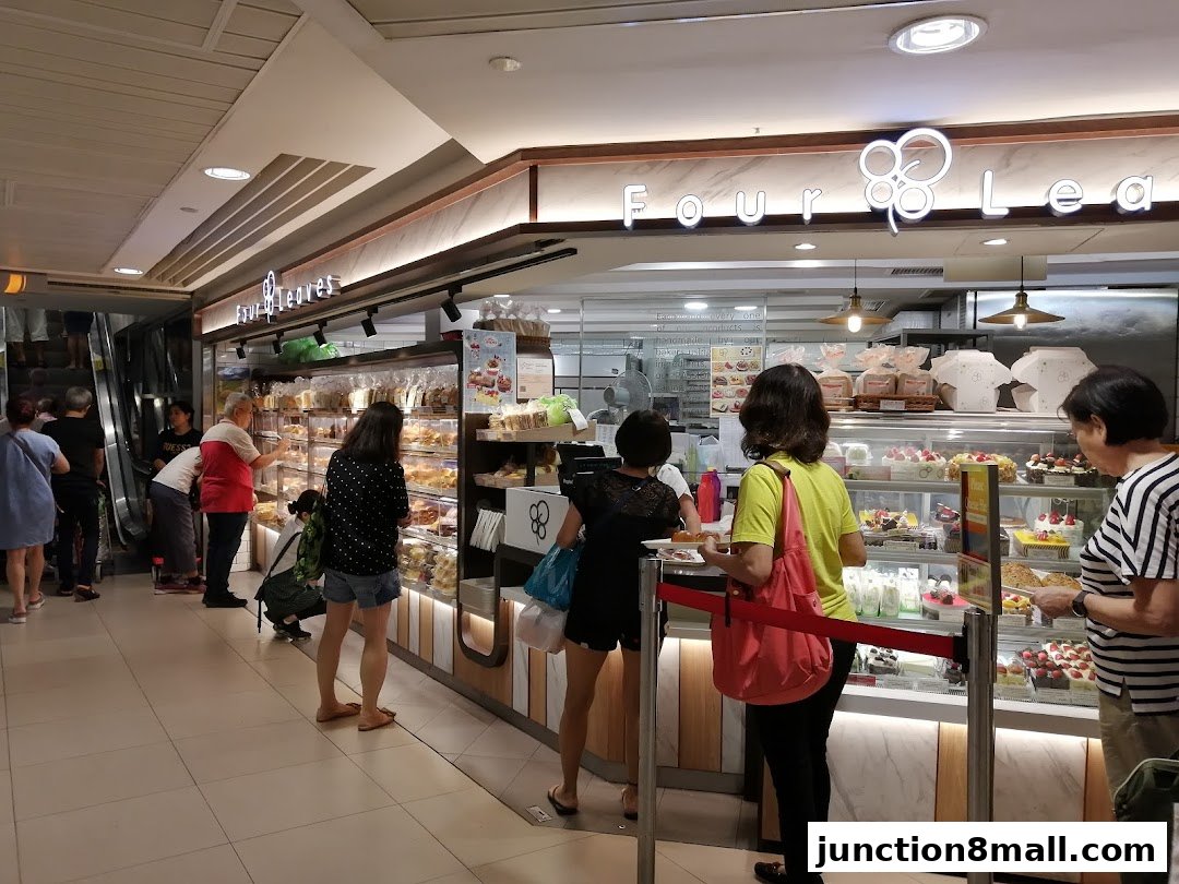 Customers are browsing and queuing at a bakery with a display of cakes and pastries.