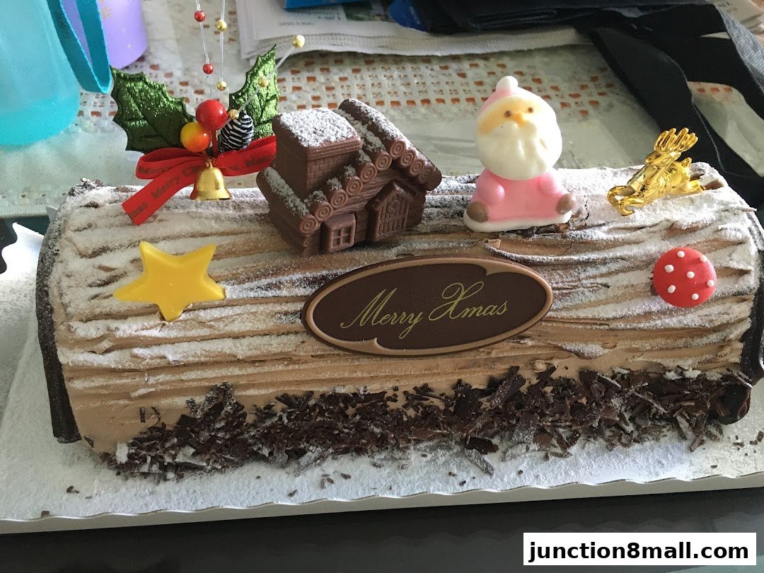 A festive Christmas log cake decorated with Santa, a house, and festive ornaments.