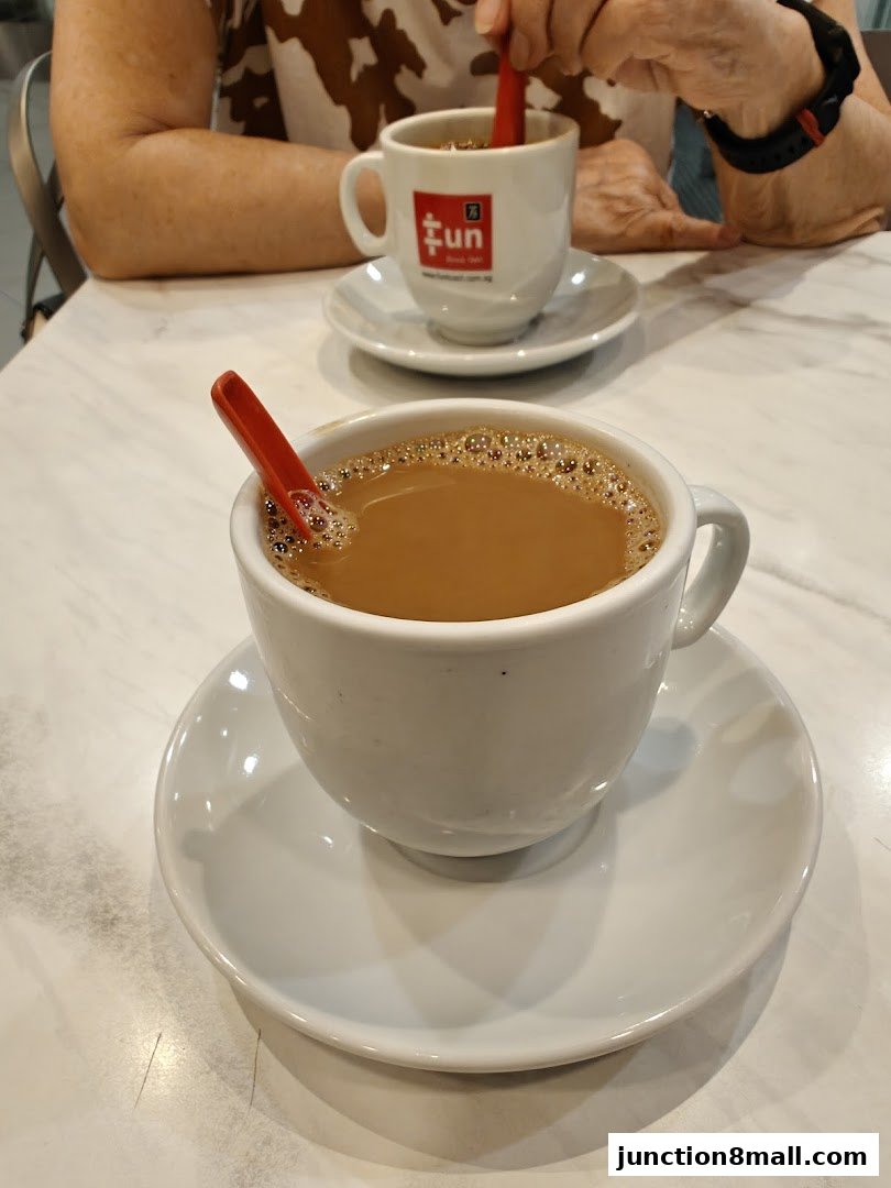 Two cups of coffee with red spoons on saucers on a marble table.