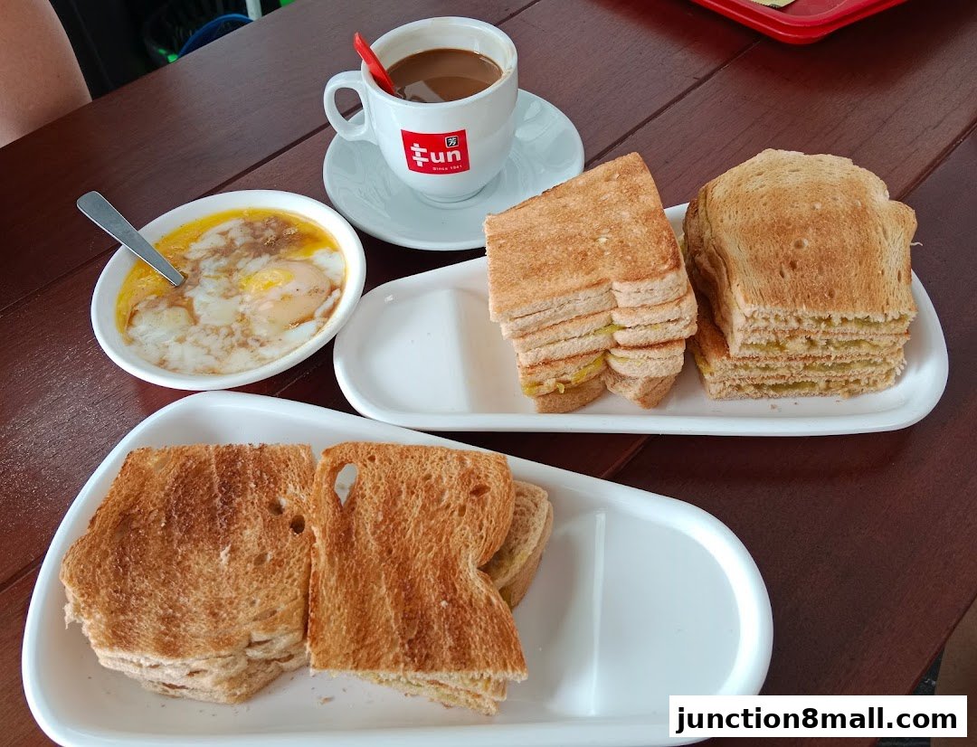 A spread of traditional Singaporean breakfast items including kaya toast, soft-boiled eggs, and coffee.