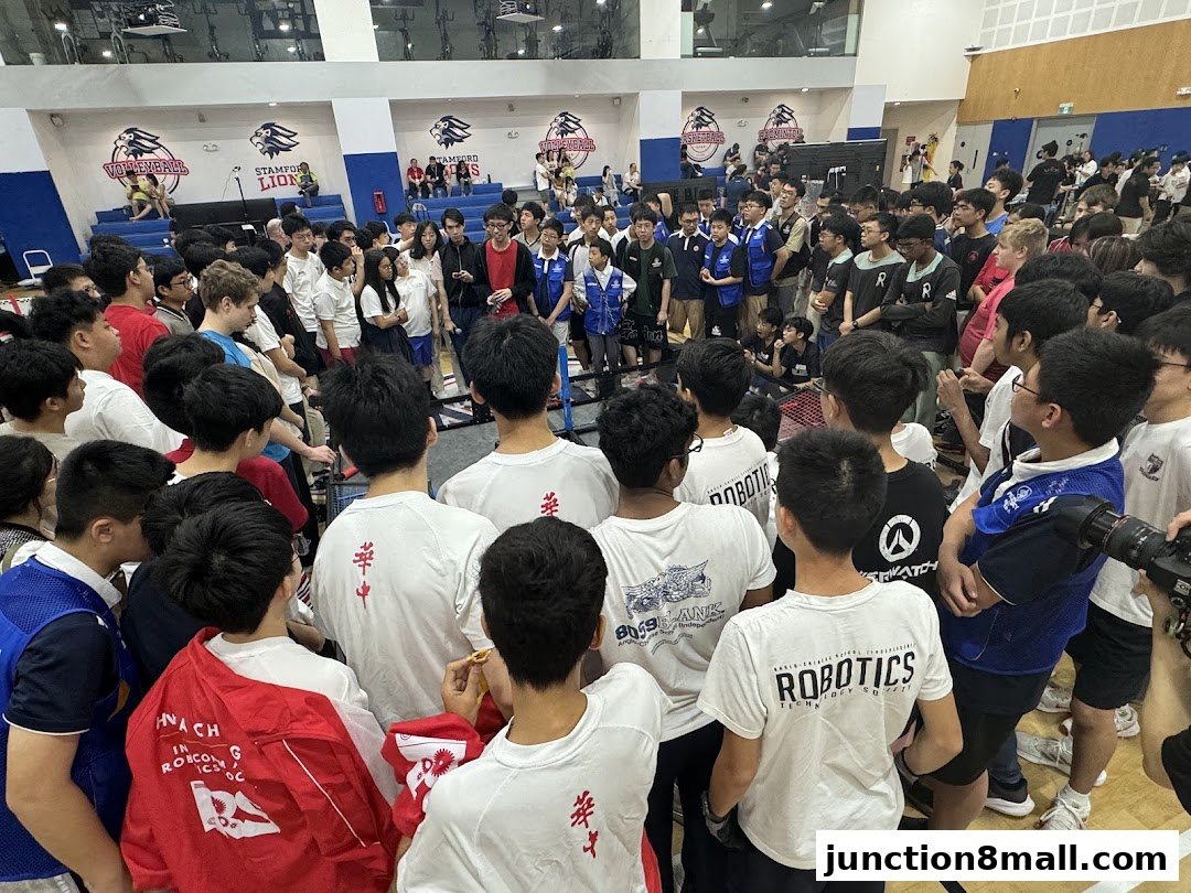 A large group of students in a gymnasium, many wearing t-shirts with 'Robotics' and other designs.