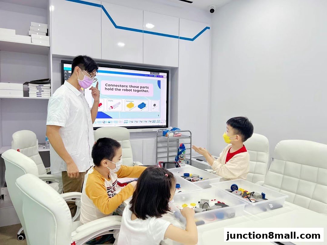 A teacher instructs children on robotics using a screen and building blocks.