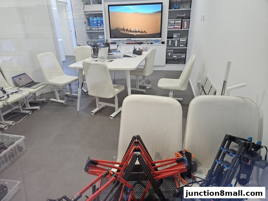 A classroom or workshop space with a table, chairs, laptops, and robotics equipment.