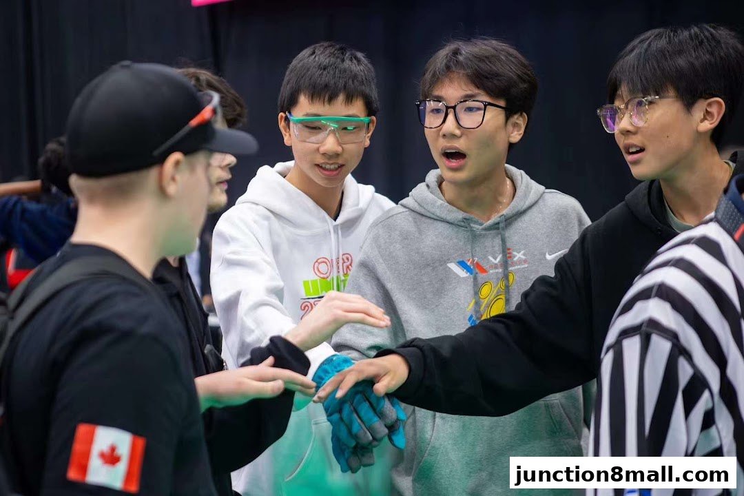 A group of young people in hoodies and safety glasses huddle together, appearing to discuss a project.
