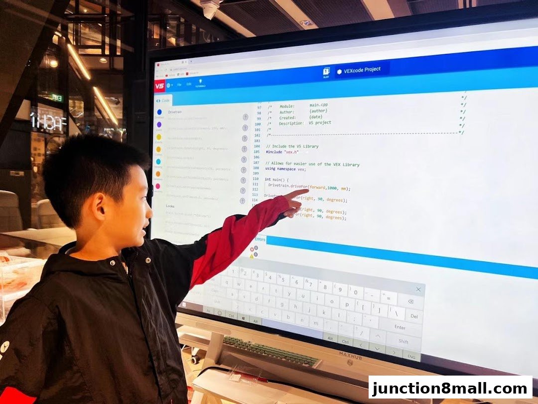 A young boy points at a computer screen displaying code for a VEXcode project.