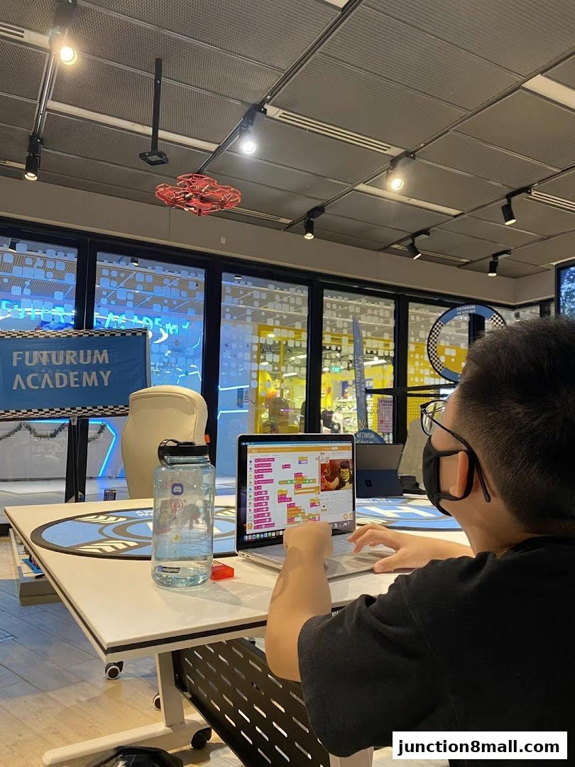 A student learns coding on a laptop at Futurum Academy, with a drone flying overhead.