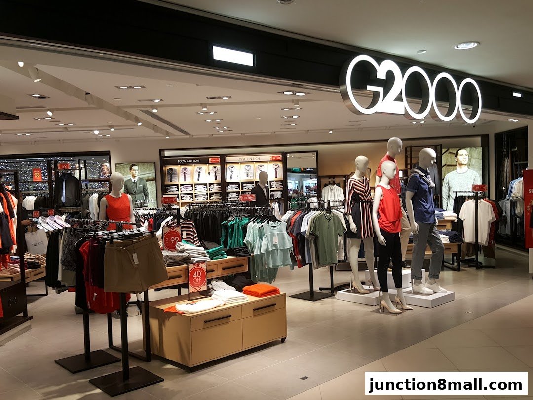 A G2000 clothing store interior with mannequins displaying outfits and racks of apparel.