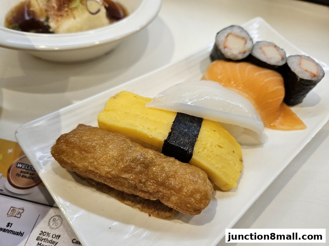 A plate of assorted sushi, including salmon, tamagoyaki, and inari, with a bowl of soup in the background.
