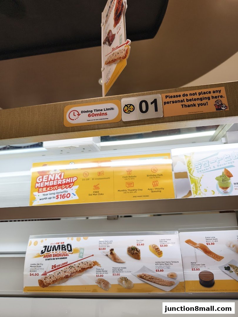 A display of various sushi items and promotions at Genki Sushi Junction 8.