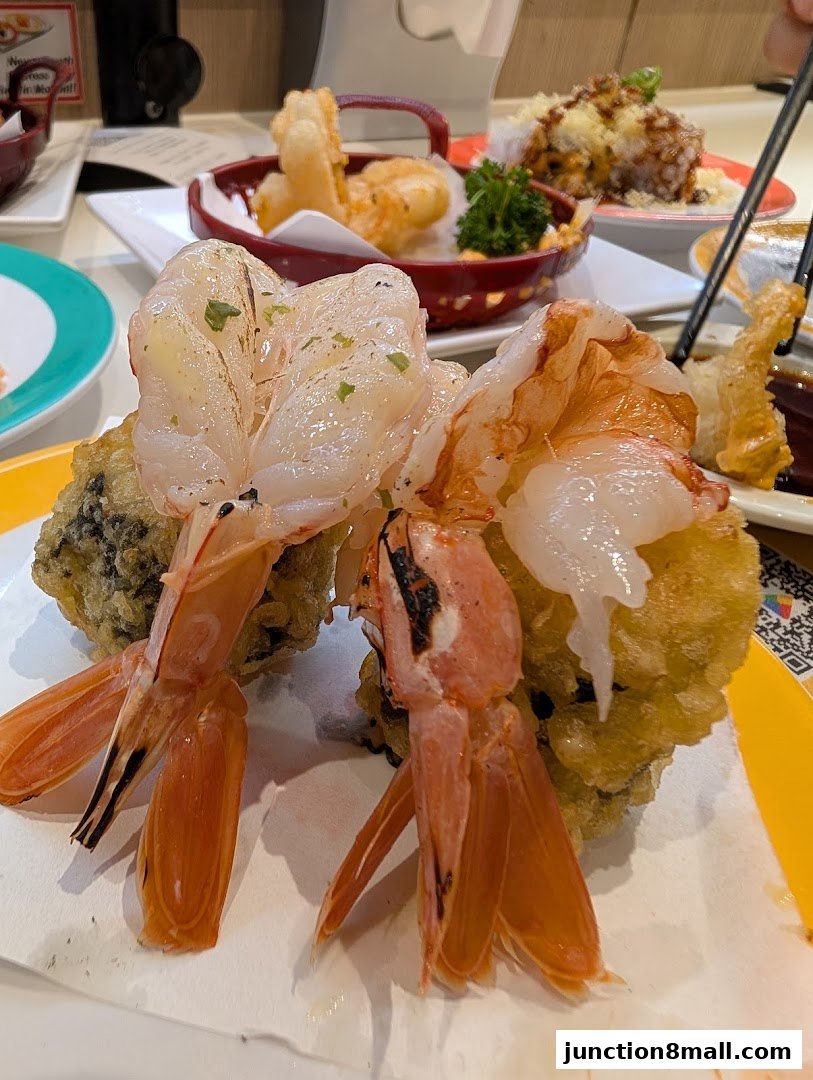 Close-up of delicious tempura shrimp and other sushi dishes on a conveyor belt.