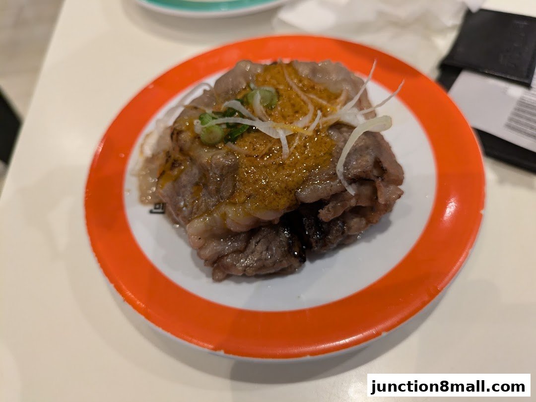 A plate of sushi with grilled beef, sauce, and green onions.