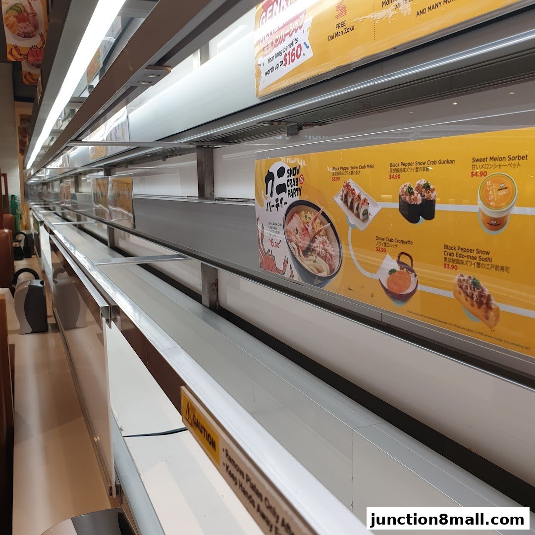 Interior view of a Genki Sushi restaurant with a conveyor belt and promotional posters.