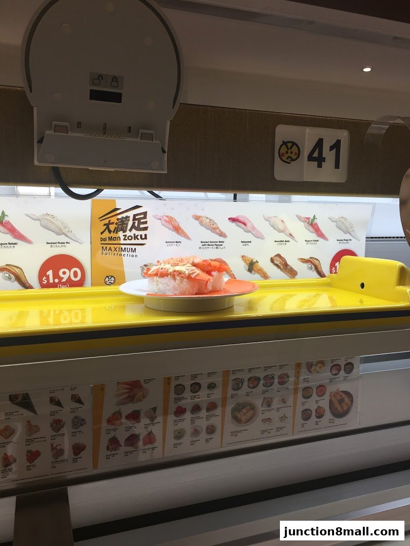 A conveyor belt sushi restaurant with various sushi dishes and a price displayed.