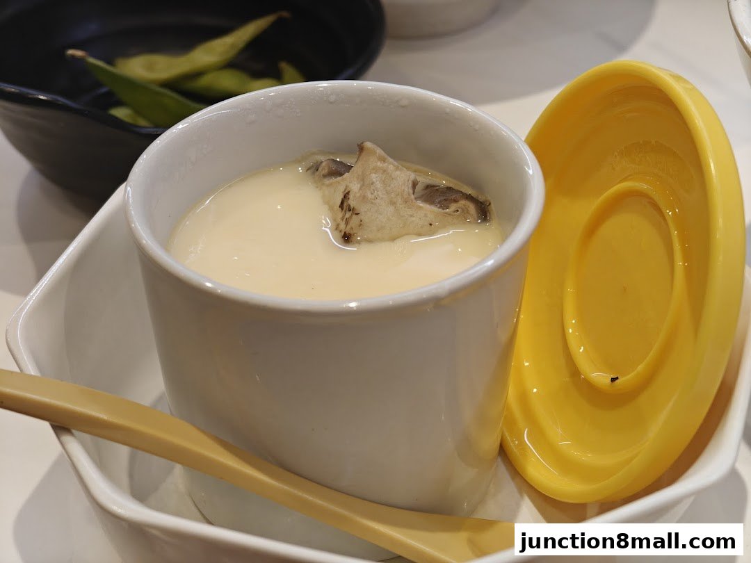 A close-up of a steaming bowl of chawanmushi with edamame in the background.