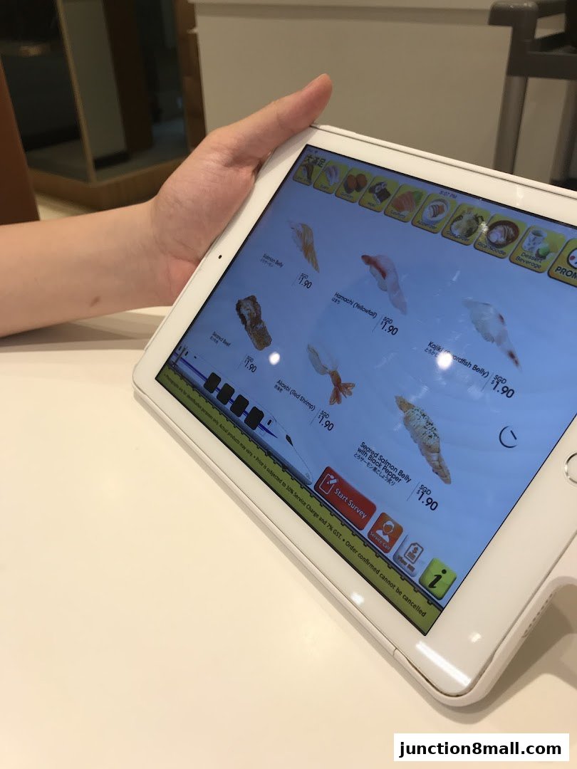 A person is holding a tablet displaying a menu of sushi items with prices.