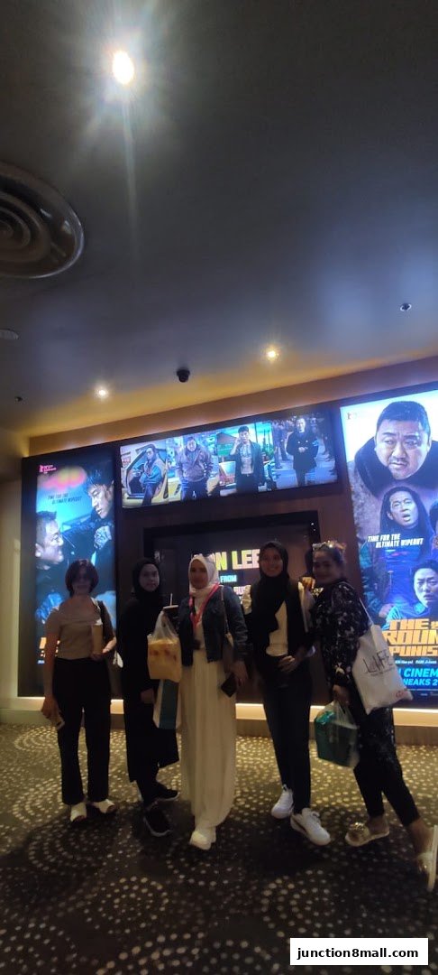A group of five women posing in front of movie posters at a cinema.