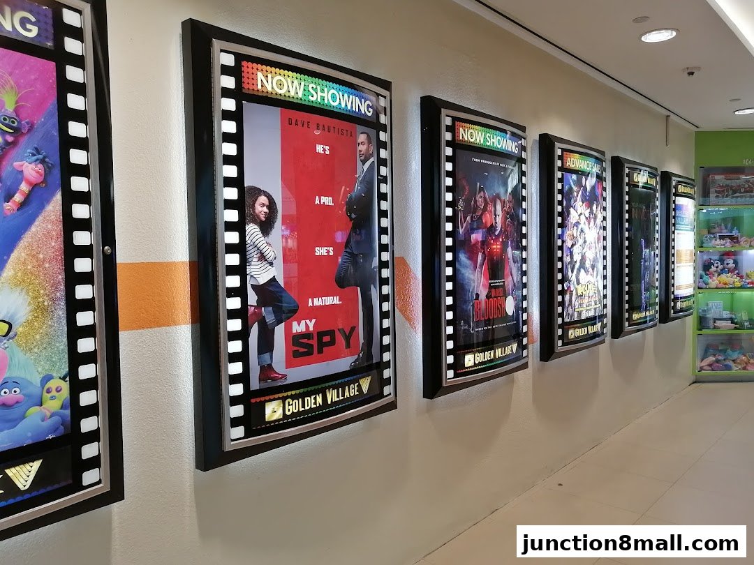 A row of illuminated movie posters displaying current and upcoming films at Golden Village Bishan.