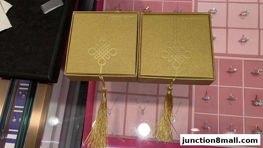 Two gold jewelry boxes with tassels displayed in front of a pink grid showcasing rings.