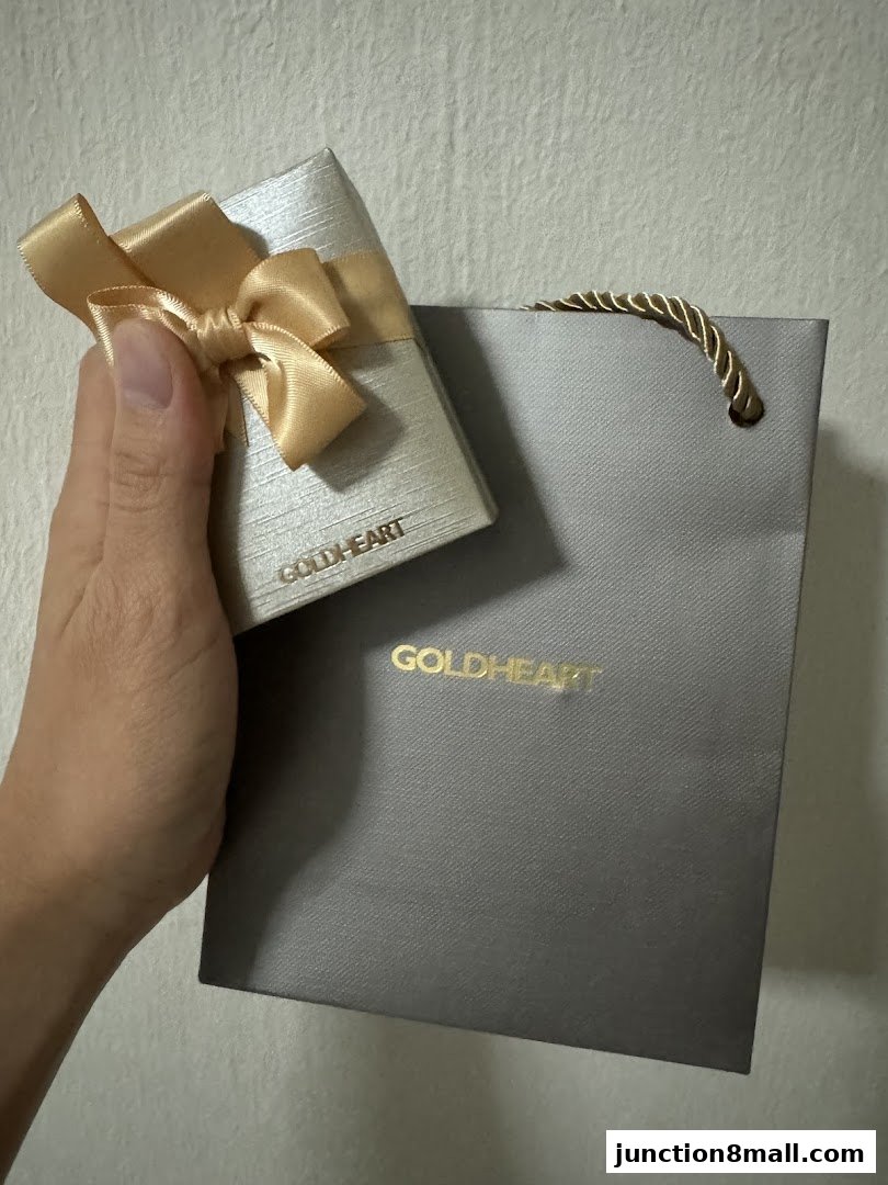 A hand holds a gold-ribboned jewelry box next to a branded shopping bag.