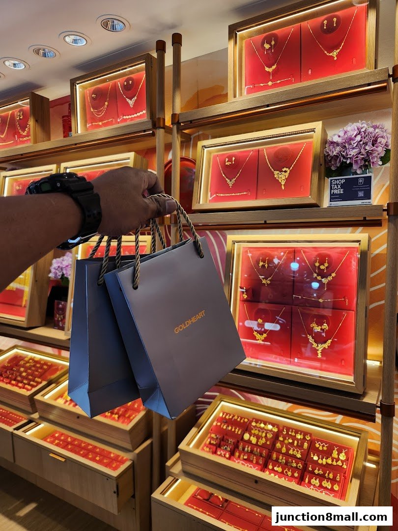 A person holds shopping bags in front of a Goldheart Jewelry display showcasing necklaces and earrings.