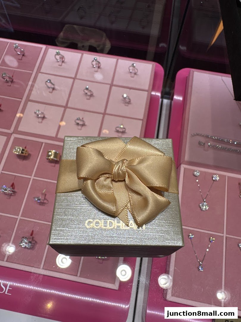 A jewelry box with a gold ribbon sits in front of displays of rings and necklaces.