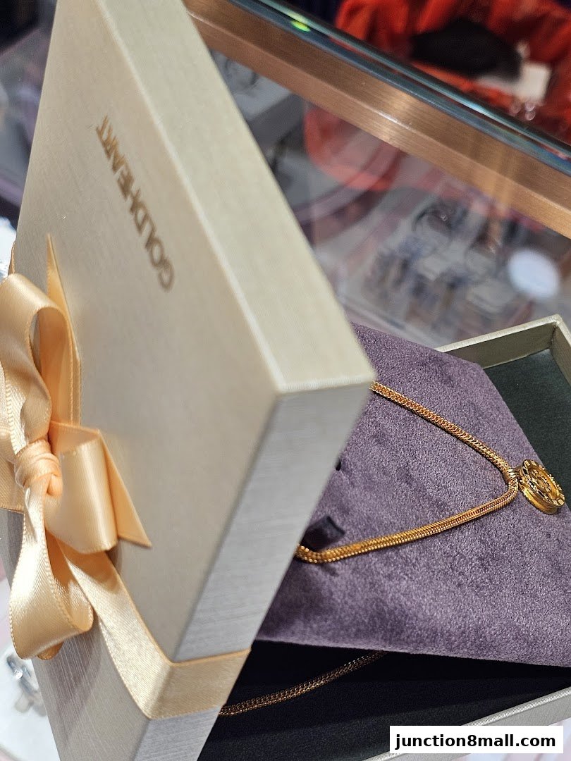 A gold necklace with a pendant in an open gift box with a ribbon.
