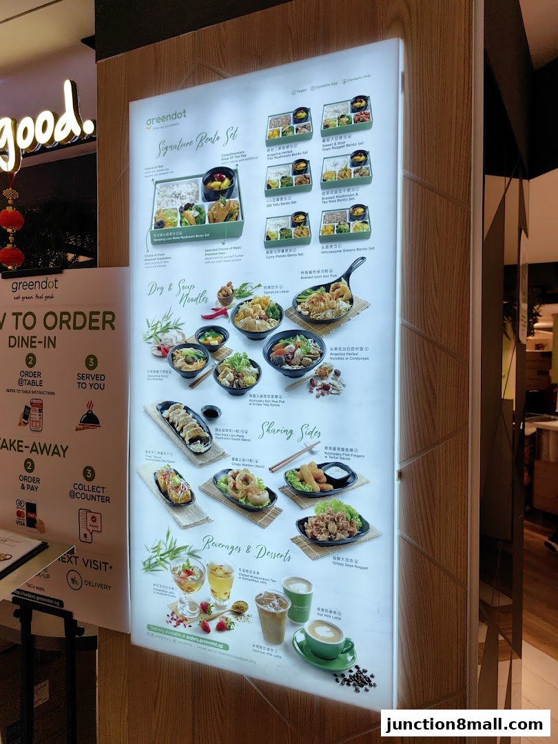 A brightly lit menu board showcasing various bento sets, noodles, sharing sides, and beverages from Greendot.
