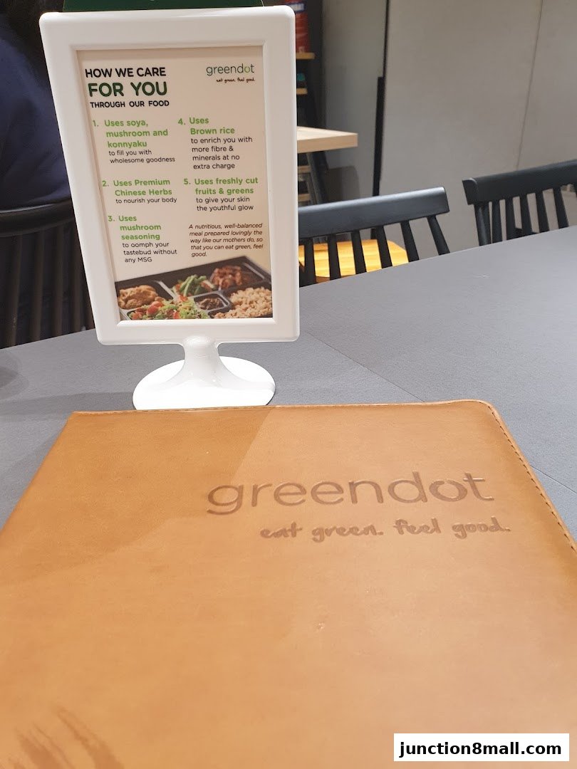 A Greendot menu and information stand on a table with chairs in the background.