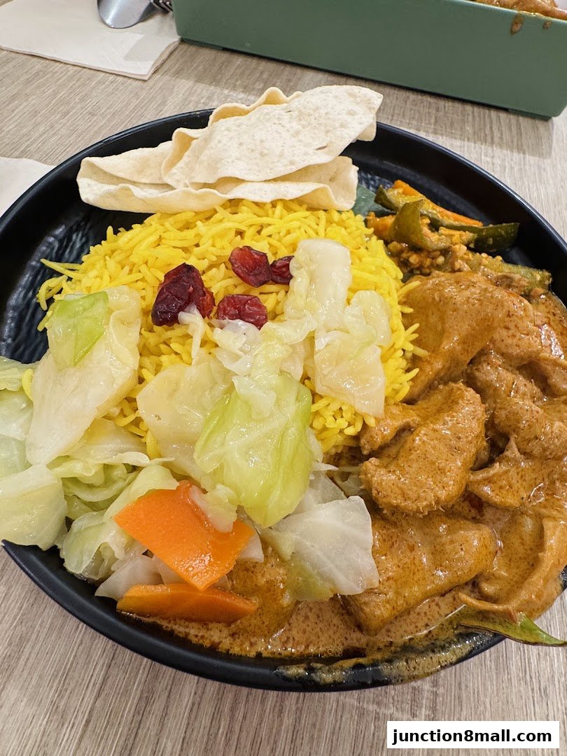 A close-up of a delicious meal featuring yellow rice, curry, vegetables, and papadum.