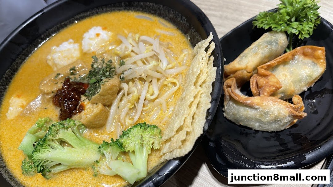 A bowl of Laksa with fried dumplings on the side, garnished with broccoli and herbs.