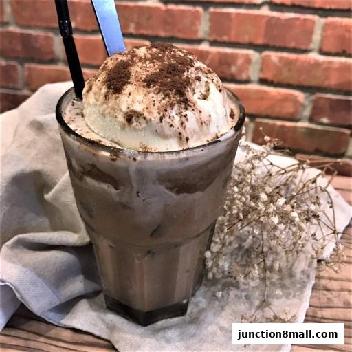 A tall glass of iced chocolate drink topped with vanilla ice cream and cocoa powder.